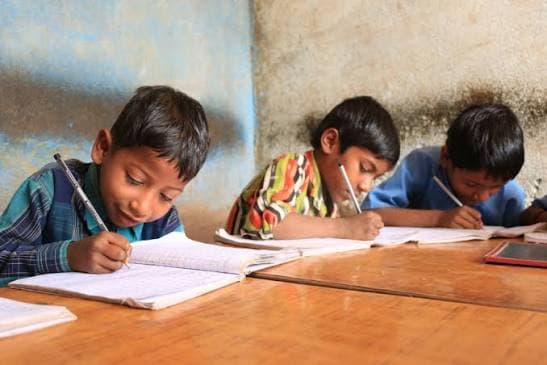 Three boys writing in exercise books at a shared desk